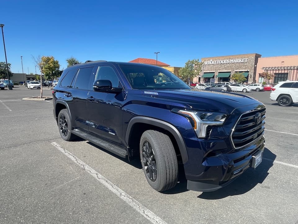 Dark blue 2026 Toyota Sequoia SUV, wide front three-quarter view outside a shopping center